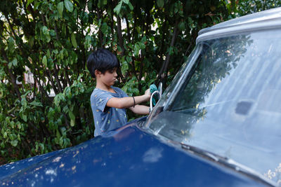 Girl with short black haircut washing mirror of blue car