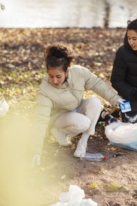 Young female environmentalist with teenager holding microplastics while crouching on land