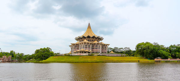 View of building by river against cloudy sky