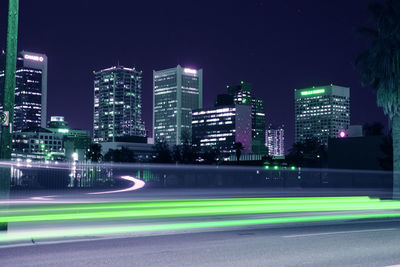 Light trails on street against illuminated buildings in city at night