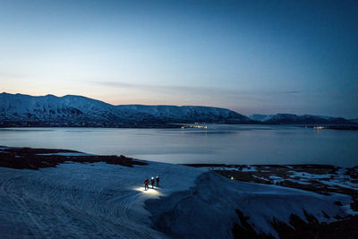 A group of 3 people skis at sunrise with ocean and mountains behind