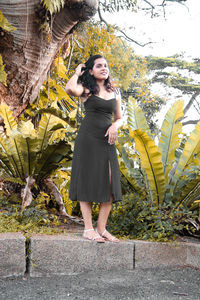 Full length portrait of young woman standing against tree