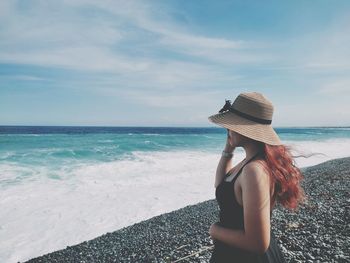 Rear view of woman standing at beach against sky