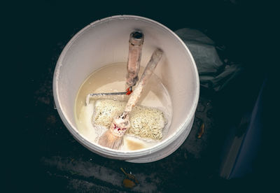 Bucket with emulsion paint and used tools for painting thrown in the street