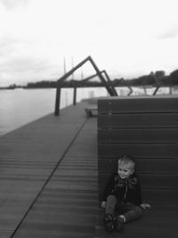 Boy sitting on pier over lake against sky