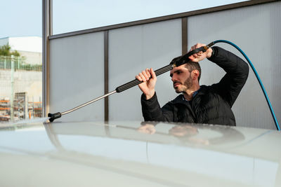 Focused man with hose washing car at washing station