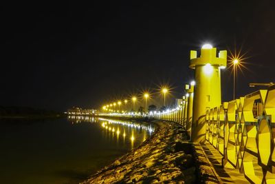 Illuminated street light by bridge against sky at night