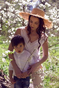 Woman in pink clothes and a straw hat stands with a child in a white shirt. blossoming apple orchard