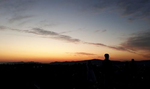 Silhouette people standing on landscape against sky during sunset