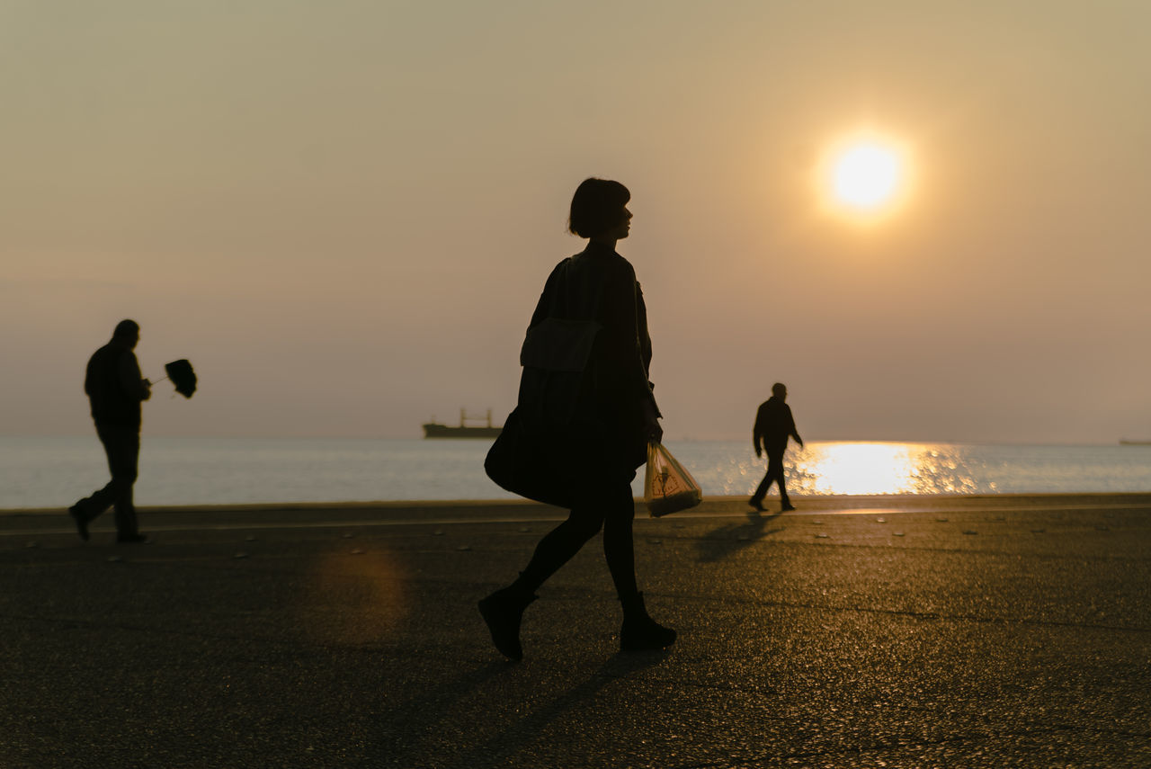 SILHOUETTE PEOPLE WALKING ON BEACH AGAINST SUNSET SKY