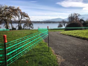 Empty park bench on field by lake against sky