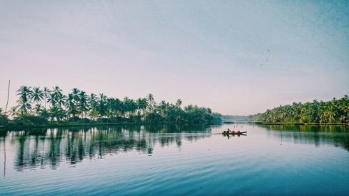 People sitting by lake against clear sky