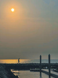 Silhouette people standing by sea against sky during sunset