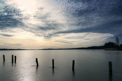 Wooden posts in lake against sky during sunset