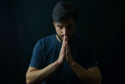 Portrait of man with hands clasped against black background