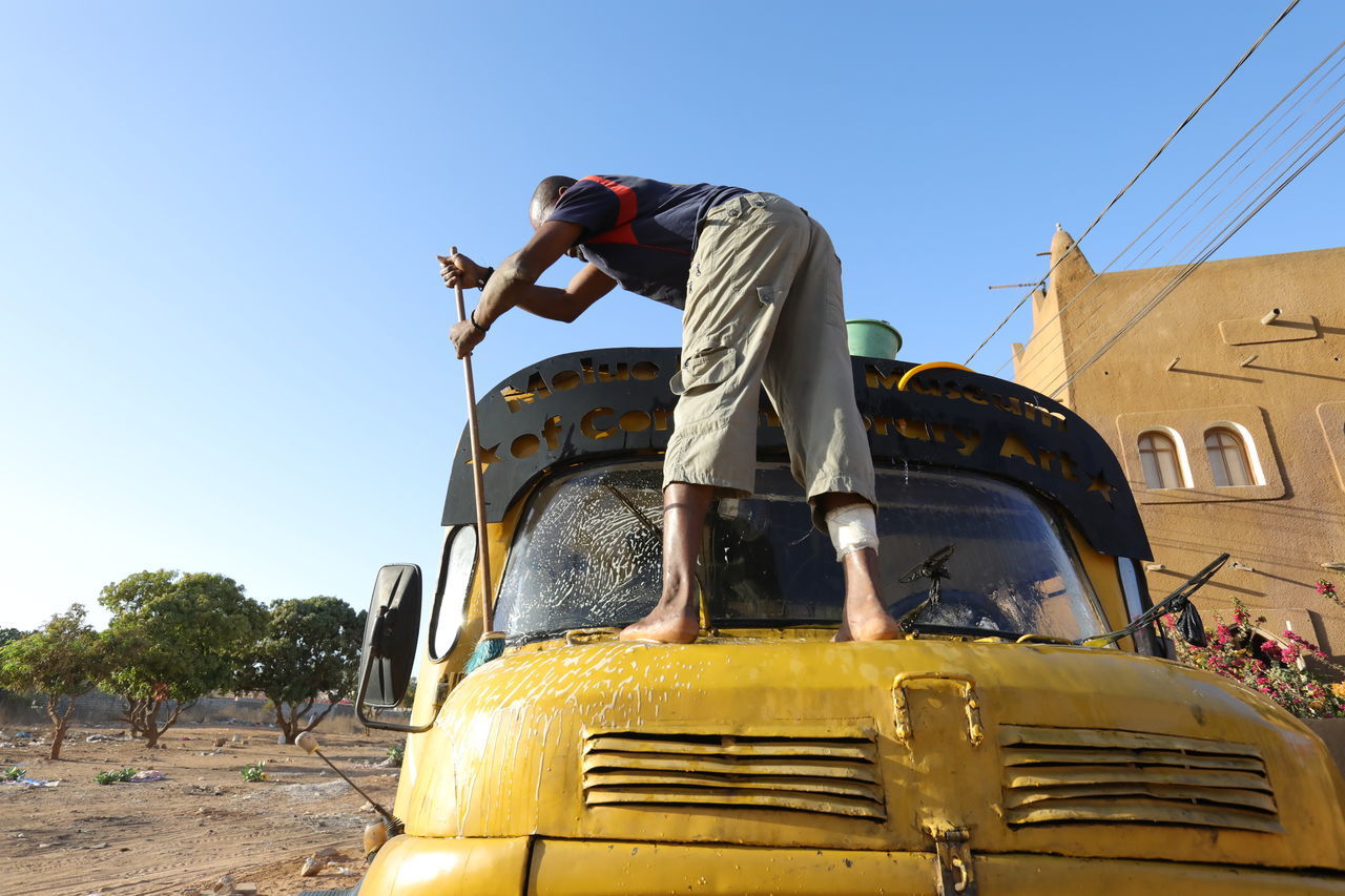 LOW ANGLE VIEW OF MAN WORKING AGAINST CLEAR SKY