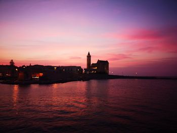 Silhouette buildings by sea against sky during sunset