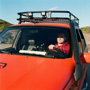 A man sits at the wheel of a car with a map and binoculars