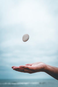 Close-up of hand catching stone against sea and sky