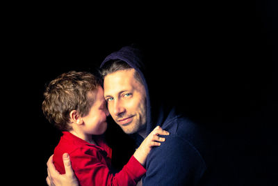 Portrait of father and son against black background