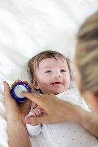 Cropped hand of woman holding cream by son on bed