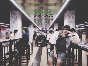 Man wearing hat and sunglasses sitting in restaurant while looking away