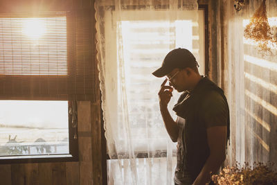 Side view of young man using mobile phone at window