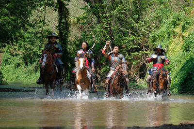Male warriors riding horses in lake at forest