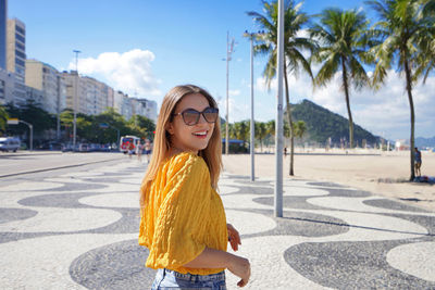 Smiling relaxed traveler woman walking along copacabana beach promenade, rio de janeiro, brazil