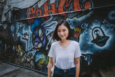 Portrait of teenage boy standing against graffiti wall