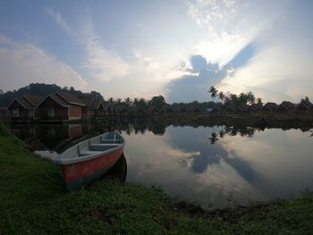 Boats moored on lake by houses against sky