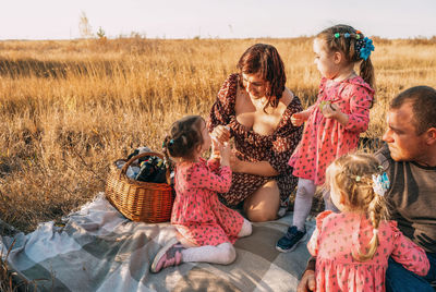 Young family with triplet girls on picnic, eco-friendly paper tubes, biodegradable materials.