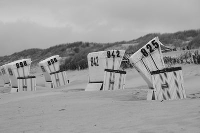 Hooded beach chairs on sand against sky