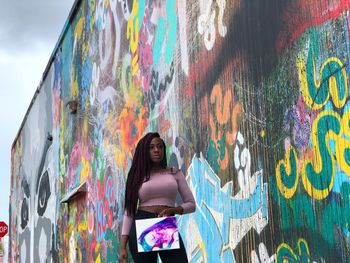 Full length of woman standing against graffiti wall