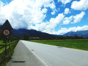 Empty road leading towards mountains against cloudy sky