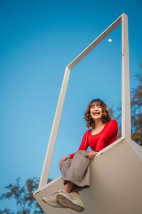 Portrait of smiling young woman sitting against blue sky