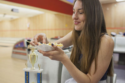 A young woman eating beside a trophy.