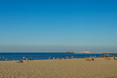 People on beach against clear blue sky