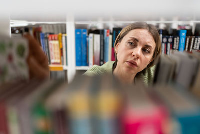 Middle-aged female choose book from bookshelf in college, university library for education research