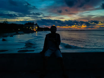 Rear view of silhouette man standing at beach during sunset