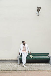 Man with laptop on bench in front of wall