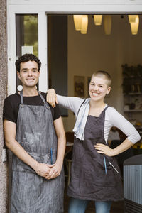 Happy female owner with hand on hip standing by male colleague at doorway