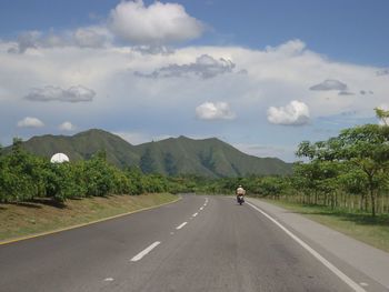 Rear view of person riding motorcycle on road by mountain against sky