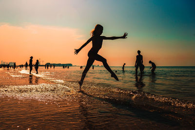 Silhouette of girl jumping on beach against sky during sunset