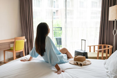 Rear view of woman sitting on bed at home