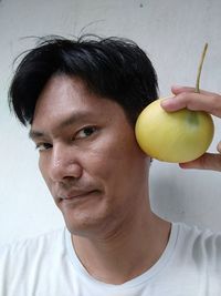 Portrait of man hearing yellow fruit against wall
