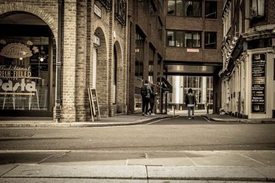 Rear view of man walking on footpath amidst buildings in city