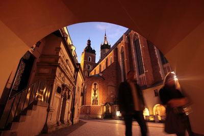 People walking on street by tunnel against wawel cathedral at dusk