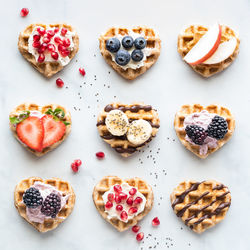 Nine mini heart shaped waffles with various cream spread and fruit toppings.