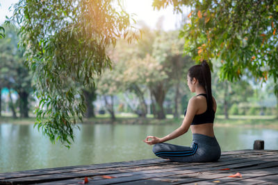 Side view of woman sitting on plant against trees